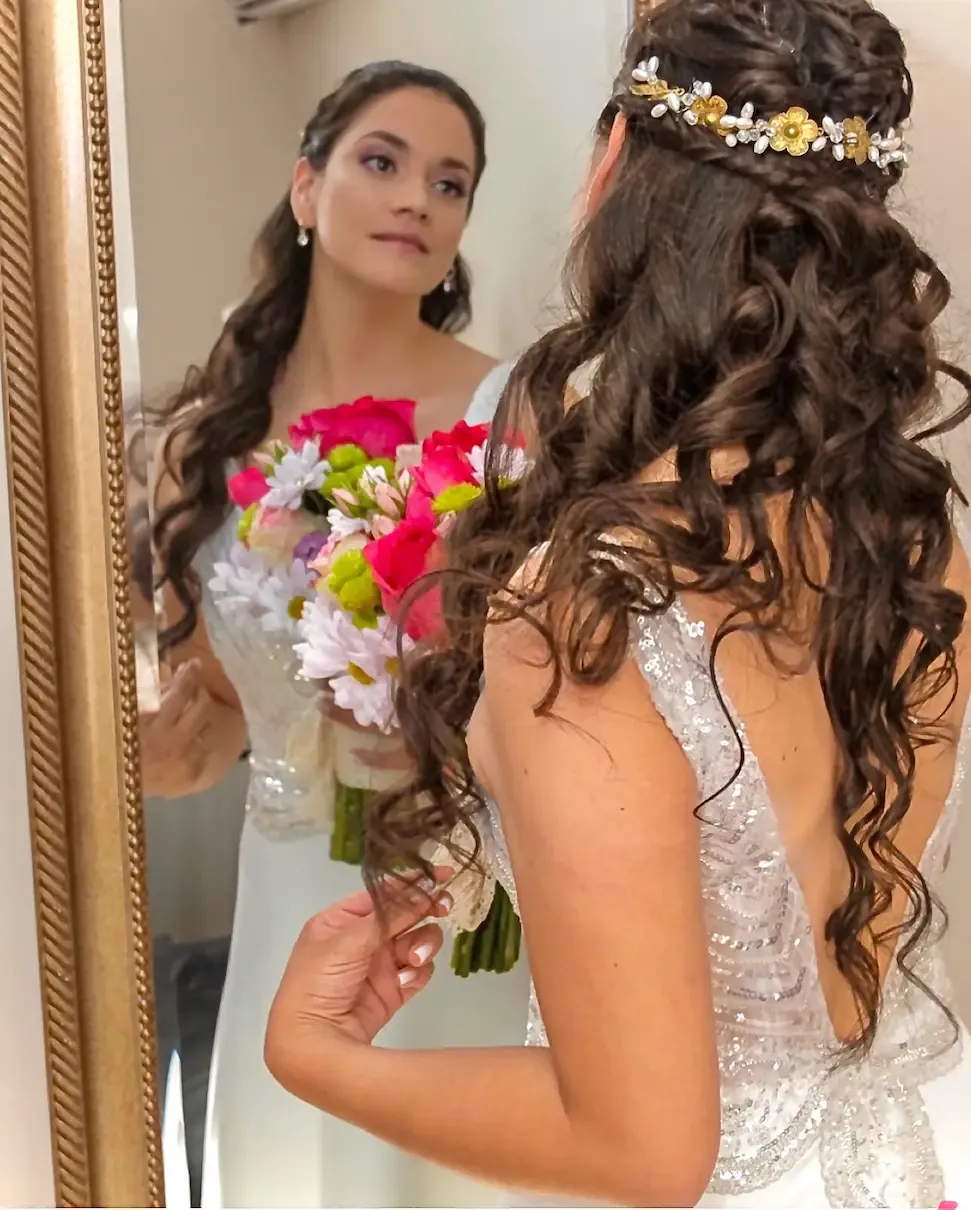 Novia con peinado semirrecogido y tocado de flores mirándose al espejo